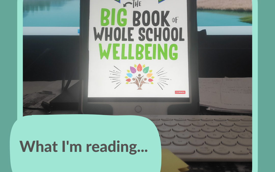 A book cover on an iPad screen in front of a computer monitor. The book title reads The Big Book of Whole School Well-being.