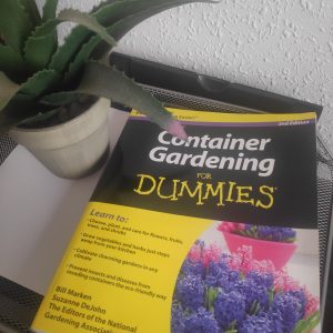 A book with the title "Container Gardening for Dummies" next to a house plant.
